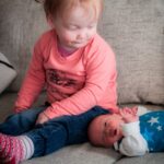 große Schwester schaut skeptisch auf die neugeborene kleine Schwester